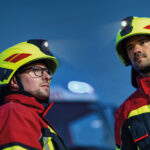 Zwei Männer tragen Feuerwehrhelm HEROS H30 mit Helmlampe HL3 Ex